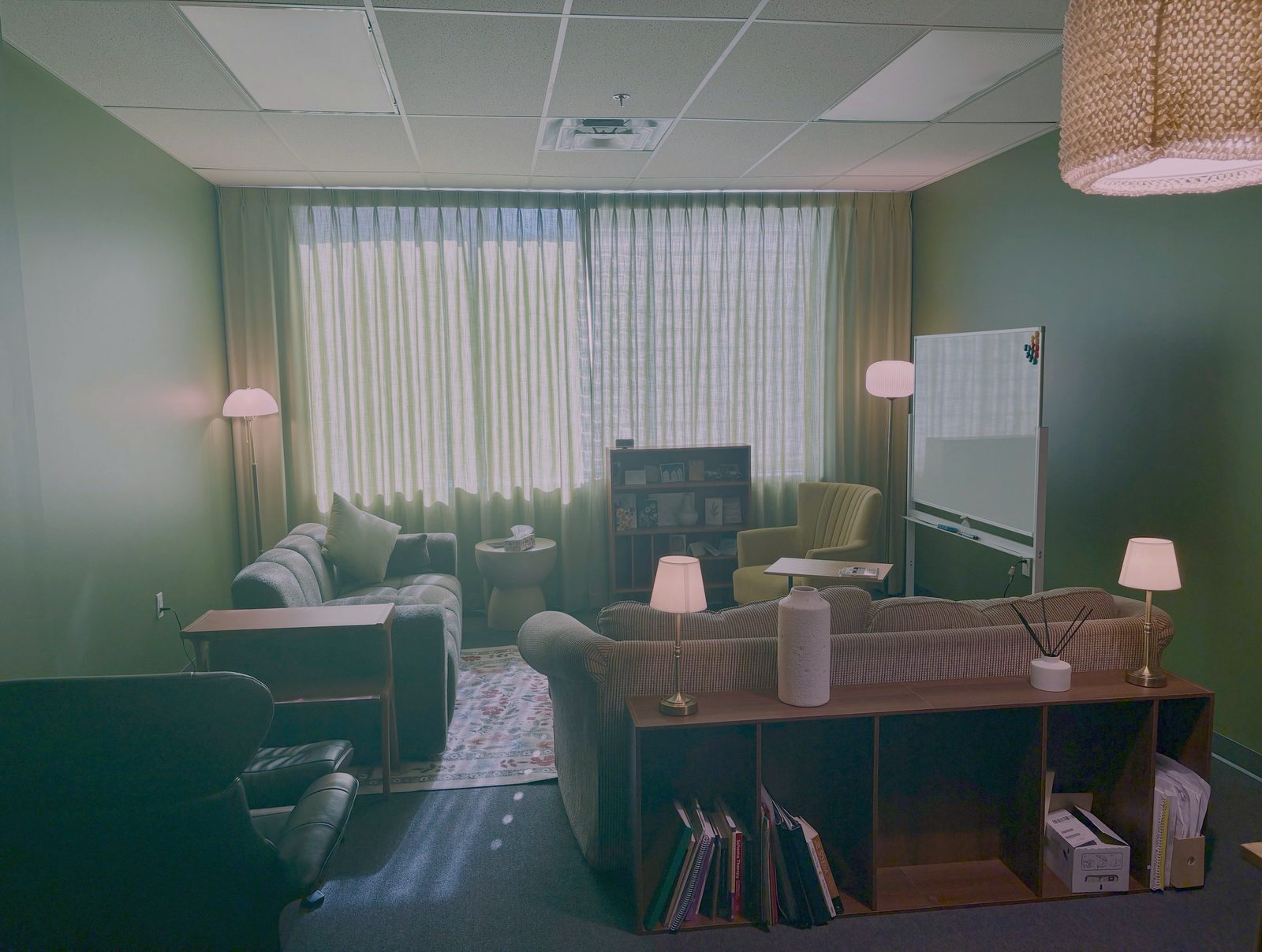 The therapy room: two sofas and an armchair around a rug, with a window behind sheer curtains